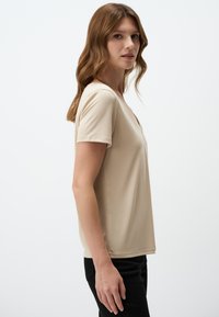 T-shirt a maniche corte color beige chiaro con scollatura a V, realizzato in tessuto morbido, caratterizzato da una vestibilità comoda e dettagli di cucitura curati.