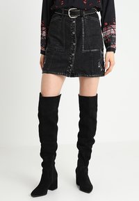 Svart denimkjol med framknappar, kontrasterande sömmar och sidofickor; stylad med knähöga svarta mockakängor.