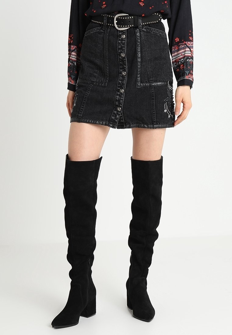 Svart denimkjol med framknappar, kontrasterande sömmar och sidofickor; stylad med knähöga svarta mockakängor.
