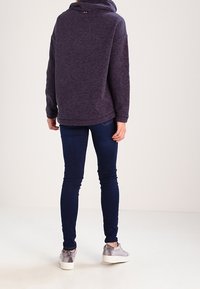 Sweatshirt viola con collo alto, vestibilità rilassata e polsini a coste. Abbinato a jeans skinny blu scuro e sneaker argentate.