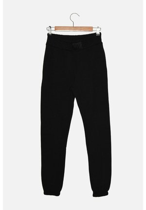 Czarne spodnie slim-fit z elastycznym paskiem i ściągaczami, wiszące na drewnianym wieszaku na białym tle.