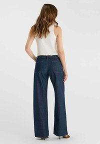 High-rise, wijde jeans in donkerblauwe denim. Heeft een minimalistisch ontwerp met twee achterzakken en subtiele stiksel details.