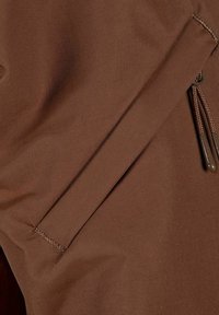 Brun lynlåslomme på et tekstureret stof med skrå ribber. Stoffet er glat, holdbart og ser ud til at være vandafvisende.