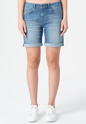 Shorts en denim bleu clair avec des revers roulés et un design classique à cinq poches. Le tissu a une texture douce et lisse. Associés à des baskets blanches.