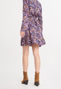 Abito floreale viola con maniche lunghe, vita arricciata e orlo a balze, abbinato a stivali alla caviglia in suede marrone con tacco a blocco.