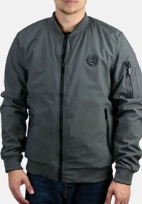 Chaqueta bomber gris fabricada en un material ligero, con cremallera frontal, puños acanalados y un parche con el logo en el pecho y el bolsillo de la manga.
