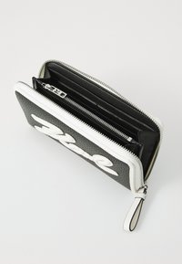 Black textured wallet with white logo, zip closure, multiple compartments, and a wrist strap. Features smooth lining and metallic hardware.
