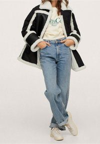 Sort faux fur jakke med hvid kant, cremet sweatshirt, lyseblå lige ben jeans og hvide sneakers. Bløde teksturer og afslappet pasform.