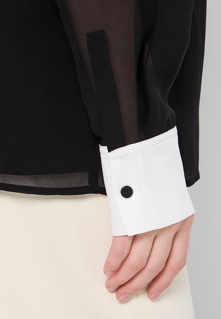 Schwarz durchscheinendes Langarmshirt mit weißem Kragen und Manschette, ausgestattet mit einem schwarzen Knopf an der Manschette und einer glatten Textur.