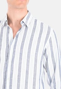 Camicia in lino con bottoni, caratterizzata da strisce verticali blu e bianche. Il colletto è rilassato, con una texture morbida e un tessuto leggero.