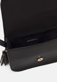 Svart faux läderväska med ett guldtonat trycklock, frynsdetalj och mjukt tygfoder. Inre märkning synlig med varumärke.