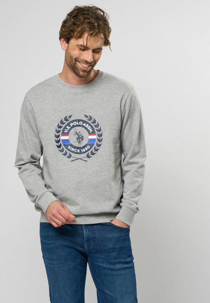 Grijze sweatshirt met een ronde halslijn, voorzien van een centrale marineblauwe graphic van een polo speler omringd door lauwerbladeren en kleurrijke strepen.