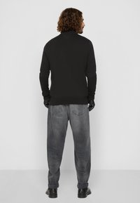 Pull noir à col montant, à texture côtelée, avec des manches longues, associé à un jean gris clair à coupe ample et des chaussures noires.