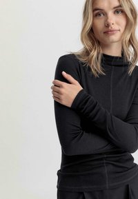 Zwarte geribbelde lange mouwtop met een hoge kraag en een aansluitend ontwerp. Heeft lichte stof en platte naden voor comfort.