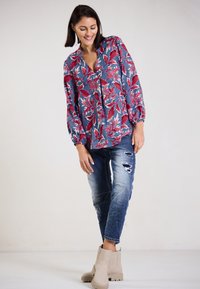 Floral long-sleeve blouse in blue with red and white leaf patterns, paired with distressed denim jeans and beige ankle boots.