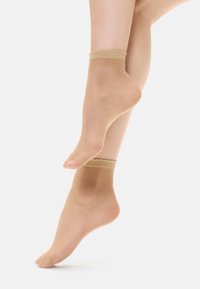 Calze alla caviglia beige trasparenti con un morbido bordo a coste. Superficie liscia con un aspetto traslucido che mette in mostra la forma del piede.