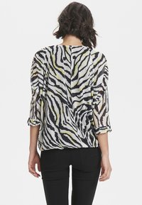 Průhledná blůza se zebřím vzorem, která má černobílé pruhy s žlutými akcenty. Rukávy jsou tříčtvrteční a design je volnější.