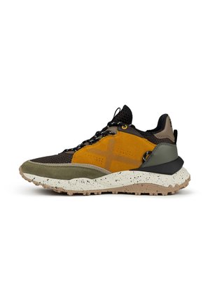 Sportschoenen in zwarte mesh en gele suede met groene suede accenten. Dikke, gespikkelde zool in beige en een textuur aan de onderrand voor grip.