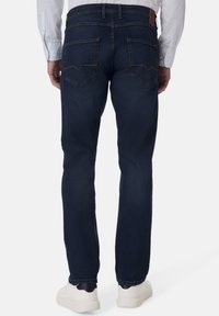 Dunkelblaue Jeans aus Denim mit schmalem Schnitt, ausgestattet mit zwei hinteren Taschen, die mit dekorativen Nähten geformt sind, und einem braunen Lederpatch an der Taille.