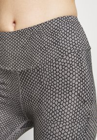 Legginsy o wysokim stanie wykonane z elastycznego materiału, z czarno-szarym wzorem przypominającym skórę węża; gładka tekstura z szerokim pasem w talii.