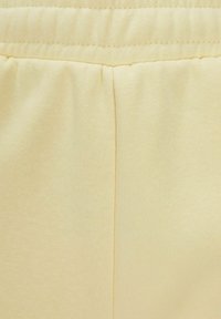 Tejido de color amarillo claro con una superficie texturizada y una cintura elástica fruncida, con una costura limpia que corre verticalmente.