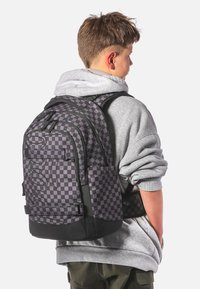 Černý a šedý kostičkovaný batoh s nastavitelnými popruhy a dvěma bočními kapsami. Má hladkou texturu a velké logo na zadní straně.