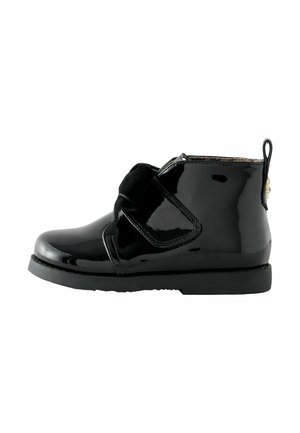 Schwarze Lackleder-Ankle Boots mit Klettverschluss, runder Zehenform, stabiler schwarzer Sohle und einer Zuglasche an der Rückseite für ein einfaches An- und Ausziehen.