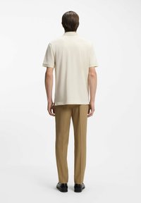 Cremefarbenes Poloshirt mit kurzen Ärmeln, getragen mit hellbrauner Hose und schwarzen Schuhen, zeigt ein sauberes, schlankes Design.