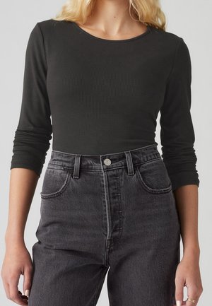 Zwarte geribbelde top met lange mouwen, gecombineerd met hooggelegen donkergrijze jeans, met knoopdetail en voren zakken. Gestructureerde stof.