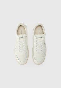 Paire de baskets basses blanches avec lacets, affichant la marque Tommy Hilfiger sur la languette, le côté et la semelle intérieure, vues de dessus sur un fond uni.