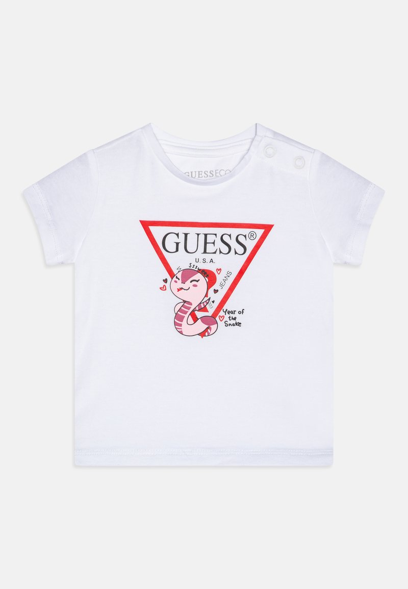 T-shirt bianco in cotone con una grafica triangolare rossa che riporta "GUESS®" e un serpente in stile cartoon, arricchita da cuori e la scritta "Anno del Serpente."
