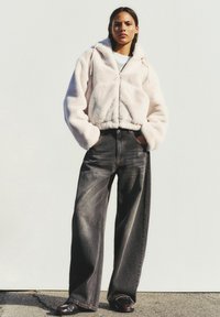 Felpa corta in faux fur rosa con zip, abbinata a jeans scuri in denim a vita alta e gamba larga. Caratterizzata da cappuccio con coulisse e vestibilità comoda.