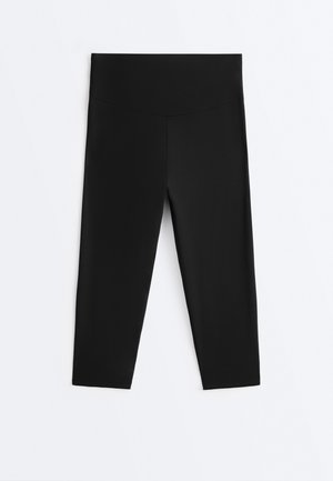 Leggings noirs taille haute coupés, avec une large ceinture, présentés à plat sur un fond blanc.
