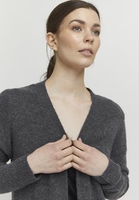 Mörkgrå cardigan i mjukt stickat material, med djup V-ringning, långa ärmar och ribbade muddarna, delvis öppen framtill.