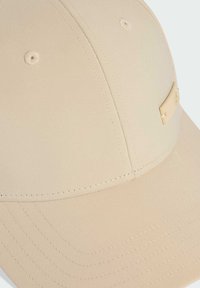 Béžová baseballová čepice s hladkým, měkkým materiálem. Obsahuje zaoblenou korunu, zvláštní švy a malou kovovou logo ozdobu na straně.