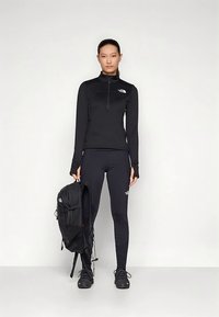 Mustast spordivarustusest koosnev poollukuga pika varrukaga topp ja keha järgivad retuusid, millele on lisatud must seljakott ja mustad jalanõud.