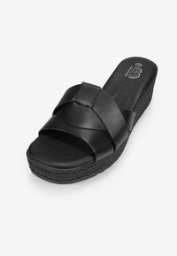 Chanclas negras con correas cruzadas anchas, hechas de cuero suave, suela de cuña texturizada con un patrón tejido y plantilla acolchada.
