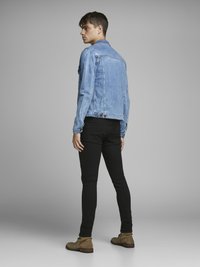 Chaqueta de mezclilla azul claro con un corte clásico, combinada con pantalones negros ajustados y botines beige. Textura suave, con un detalle mínimo.