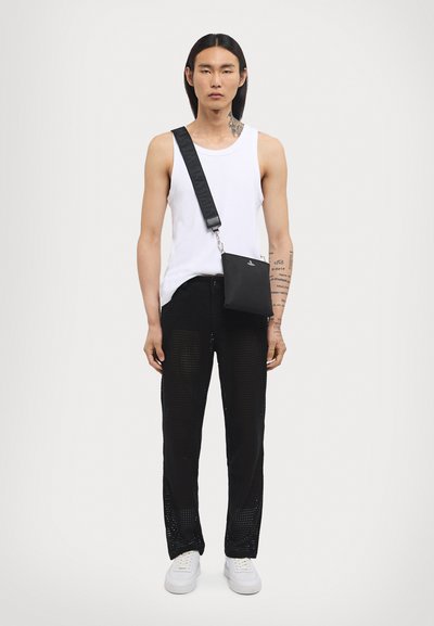 Čierne sieťované nohavice s viditeľným vzorom, biele tielko a čierna crossbody taška. Biely tenisky dotvárajú outfit. Jednoduchý dizajn, voľný strih.