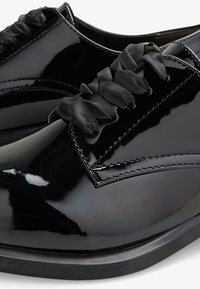 Black patent leather shoes with glossy finish, featuring ribbon laces and accent stitching. Rounded toe and low-profile design.
