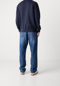 Námořnická mikina s žebrovanými manžetami, spárovaná s volnými modrými džínami s kapsami na zadní straně a zúženými lemy. Bílé tenisky s béžovými podrážkami.