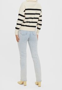 Sweter w paski w kolorze kremowym i czarnym, zestawiony z jasnoniebieskimi dżinsami. Dżinsy są dopasowane i lekko zwężane, posiadają klasyczne kieszenie.