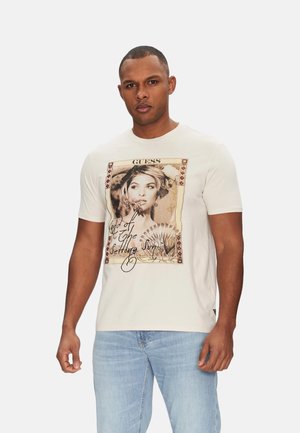 Camiseta de algodón crema con un estampado gráfico del retrato de una mujer con acentos florales y texto. Mangas cortas y cuello redondo.