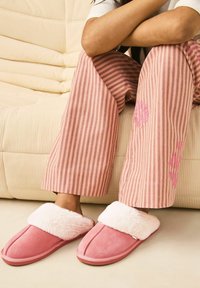 Pink suede slippers with a white faux fur cuff, paired with pink and white striped pajama pants featuring a floral pattern.