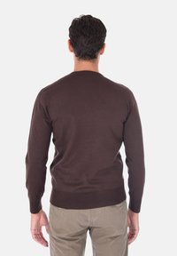 Maglione a maglia marrone con polsini a coste, caratterizzato da un classico collo rotondo e un design aderente, indossato sopra pantaloni chiari.