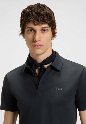 Black polo shirt with a collar, featuring a small gray "BOSS" logo. The model wears a dark scarf tied around the neck. Short sleeves.