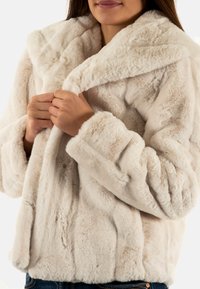 Crème-kleurige nepbontjas met een brede kraag, textuur oppervlak en verborgen sluitingen, met een boxy pasvorm en lange mouwen.