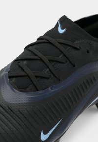 Svart idrottssko med en texturerad ovandel, mörka snören och en blå Nike-logotyp. Designen inkluderar segmenterade mönster på sidorna.