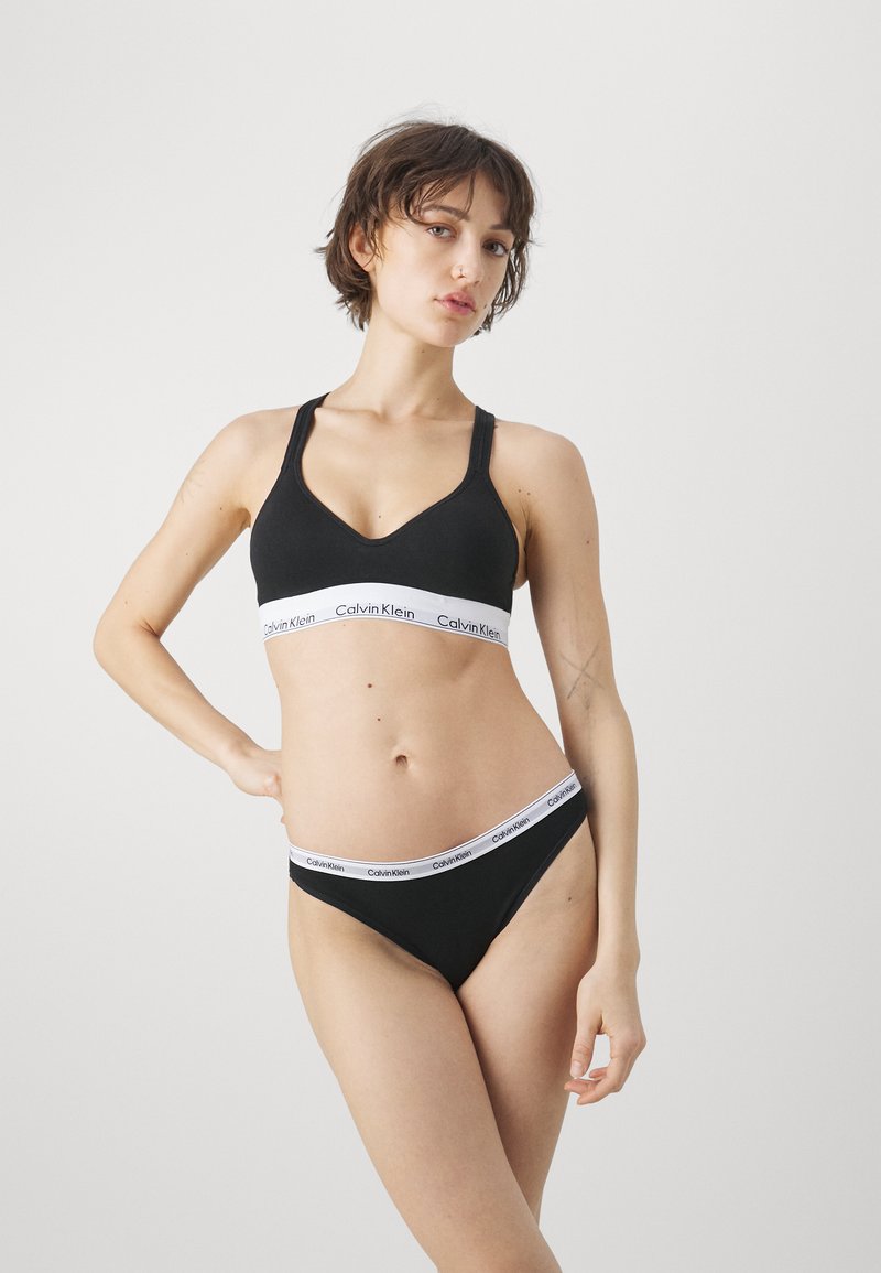 Zwarte katoenen bh en stringset met elastische witte tailleband met "Calvin Klein" logo, gladde textuur en eenvoudig ontwerp.