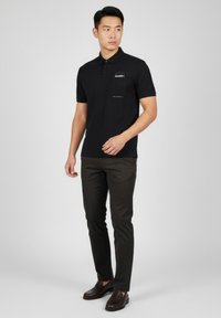 Musta lyhythihainen poolopaita, jossa on rintatasku ja hillitty logo. Yhdistetty tummiin, kapeisiin housuihin ja loafereihin.